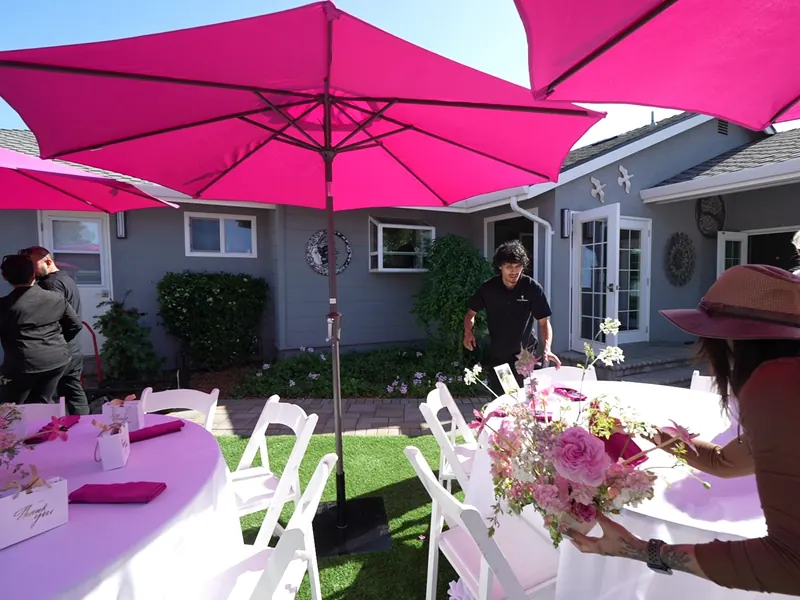 Team member carrying a floral centerpiece to a shaded outdoor table