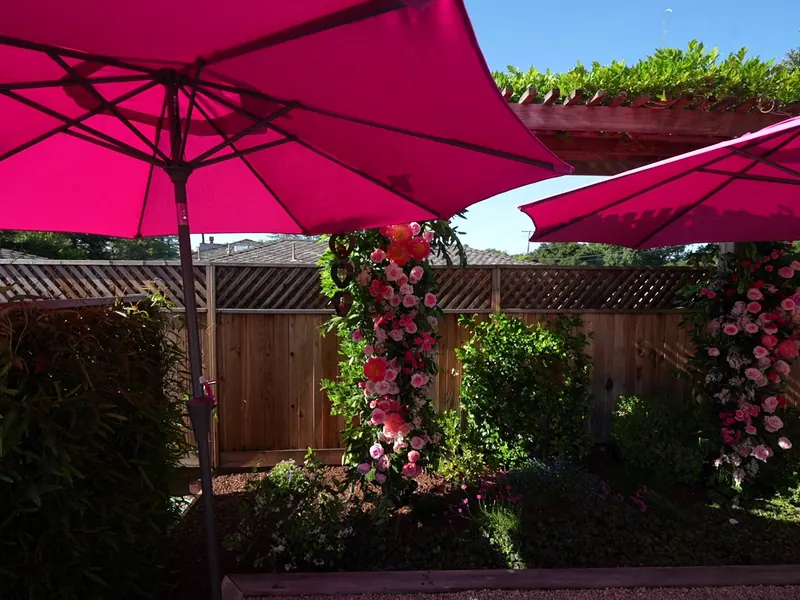 Floral arch and pink umbrellas set up in a backyard for a party
