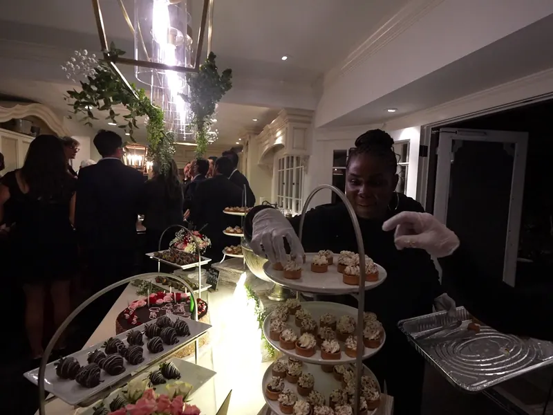 Attendant handing desserts to guests beside a lit dessert display