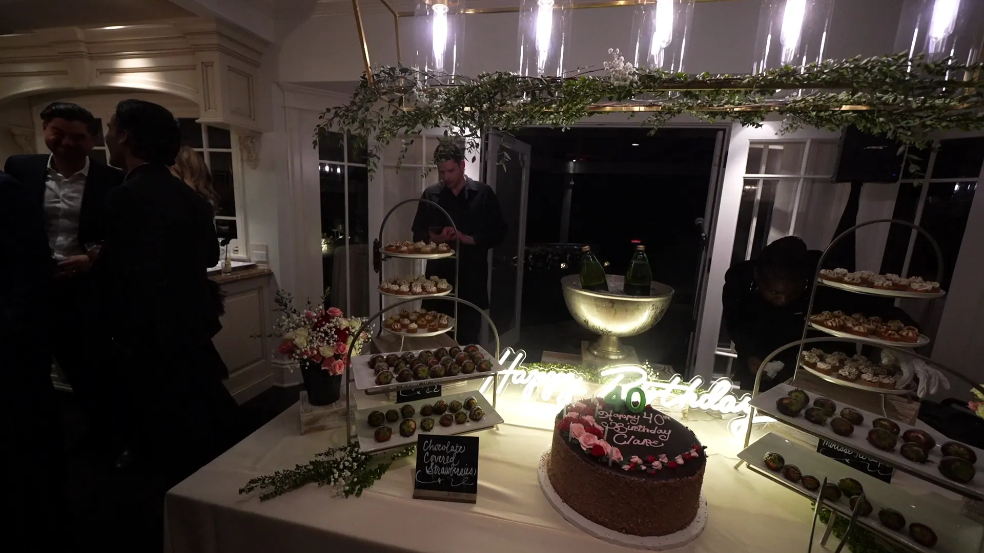 Birthday cake and tiered dessert tower under hanging greenery