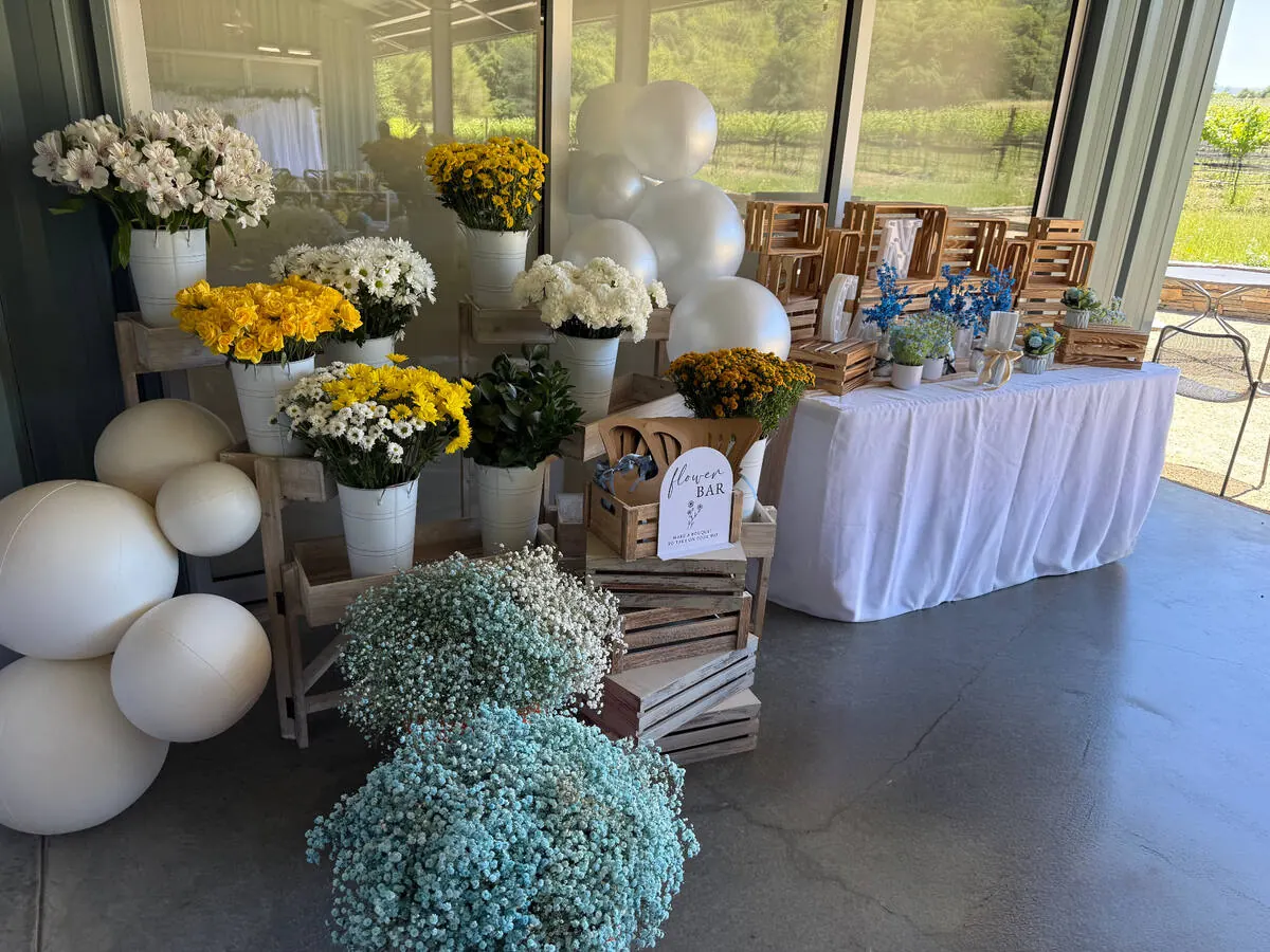 Bloom bar stocked with yellow roses, daisies and baby's breath beside ribbon and wrapping paper for guests to build bouquets — signature bloom bar for Tri-Valley catering